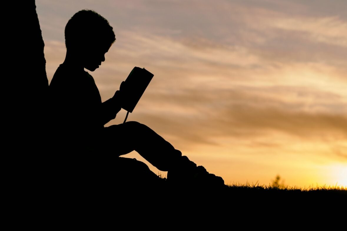 silhouette of child sitting behind tree during sunset