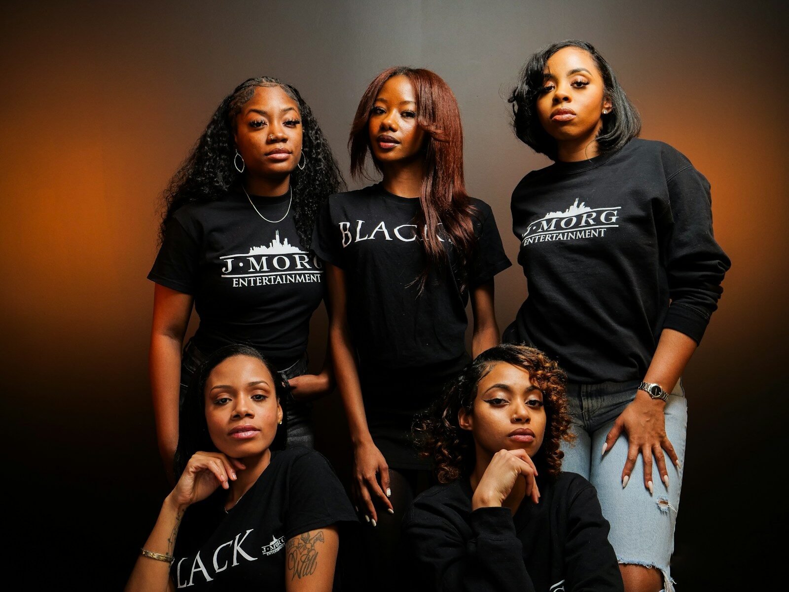 Five young women in black t-shirts pose together.