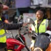 Two M-KOPA field agents in safety vests talk beside motorbikes on a Nairobi street