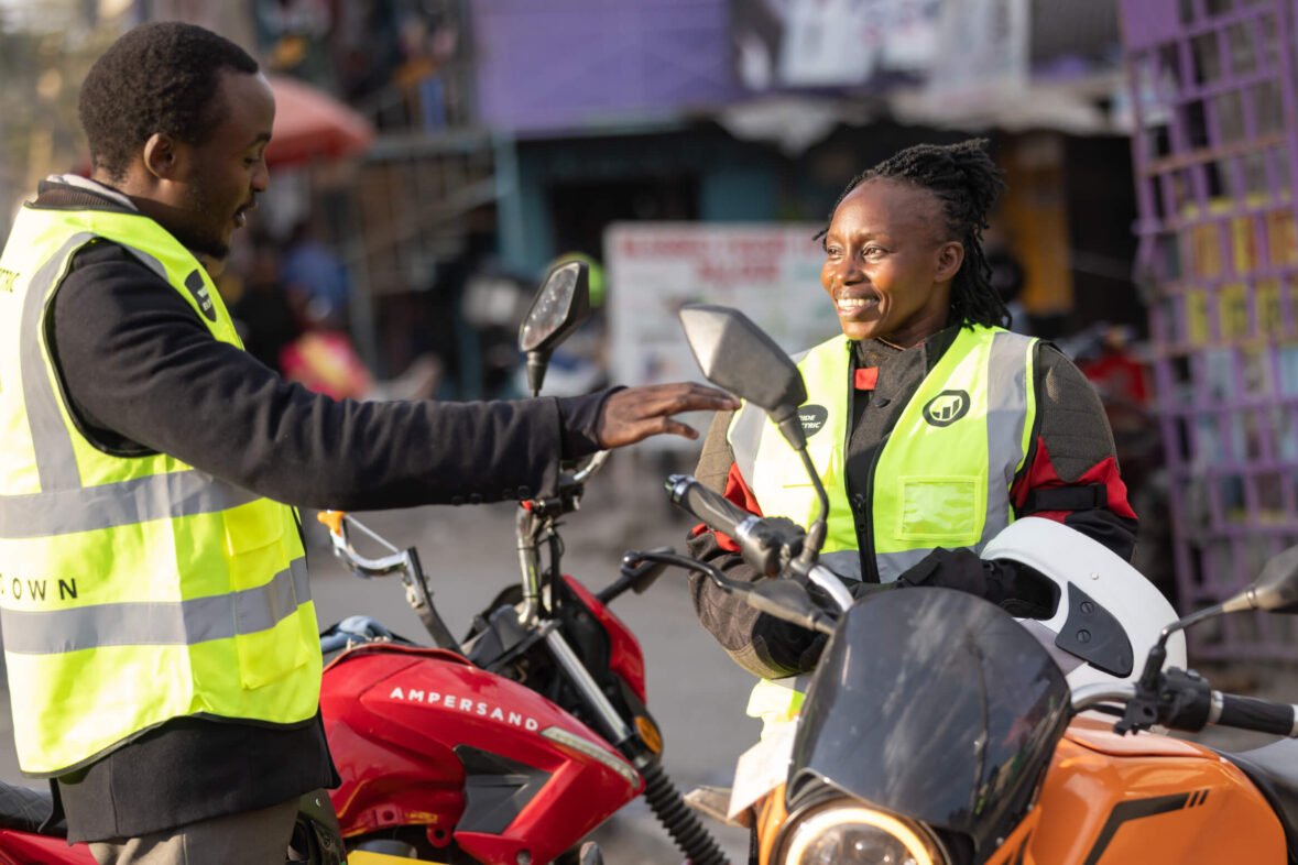 Two M-KOPA field agents in safety vests talk beside motorbikes on a Nairobi street
