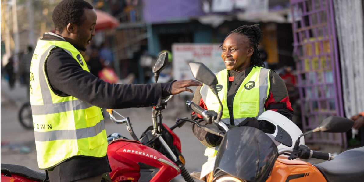 Two M-KOPA field agents in safety vests talk beside motorbikes on a Nairobi street